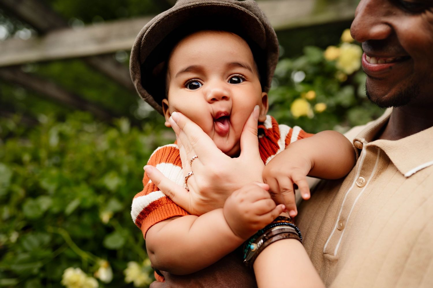 Playful baby wearing orange shirt and cap makes silly face during photography session with raleigh newborn photographer