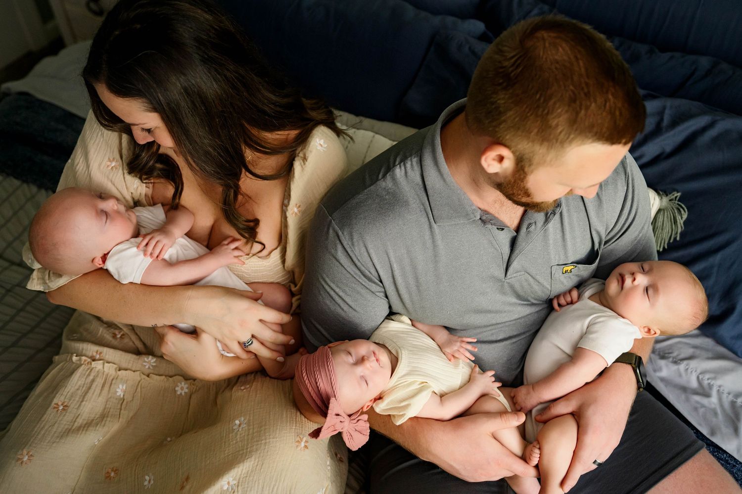 Parents hold triplet newborns and share a tender moment during newborn photography session with raleigh newborn photographer