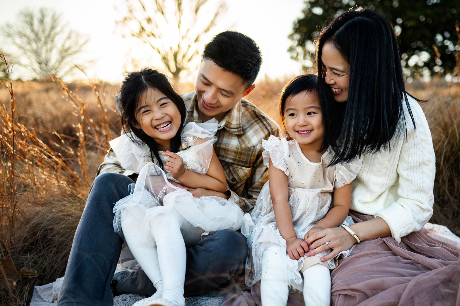 A family sits together outdoors during golden hour in a natural field with tall grass during outdoor family photography session in raleigh