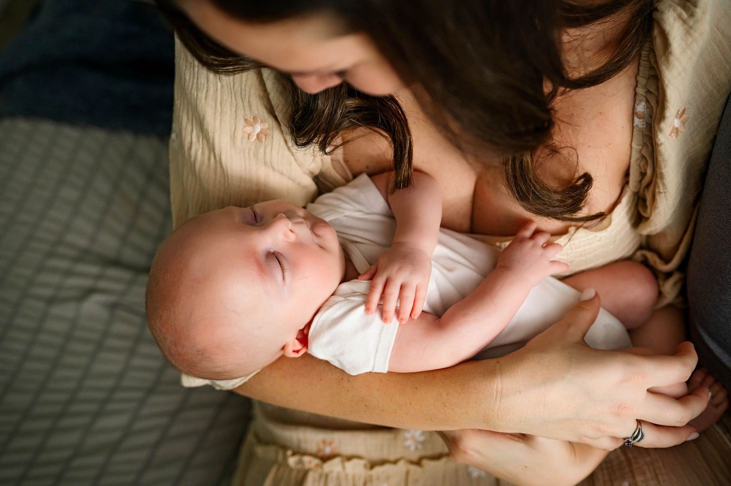 Mother in white gazes lovingly at a sleeping newborn cradled in her arms with raleigh newborn photographer Emma Branch Photography
