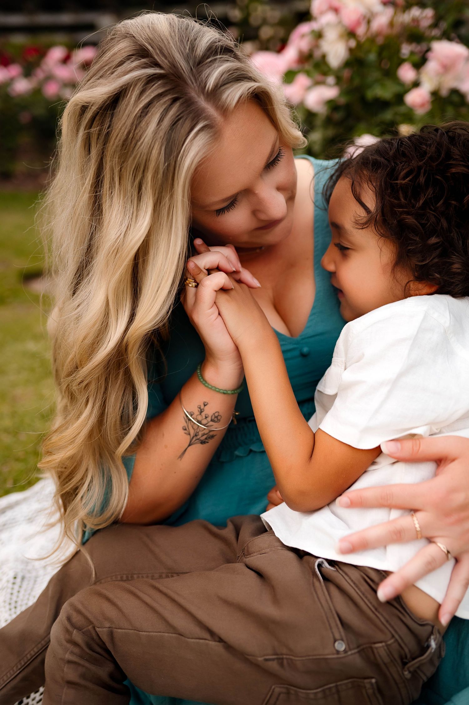 A tender moment between mother and son sharing affection outdoors with pink flowers blooming with wake forest maternity photographer