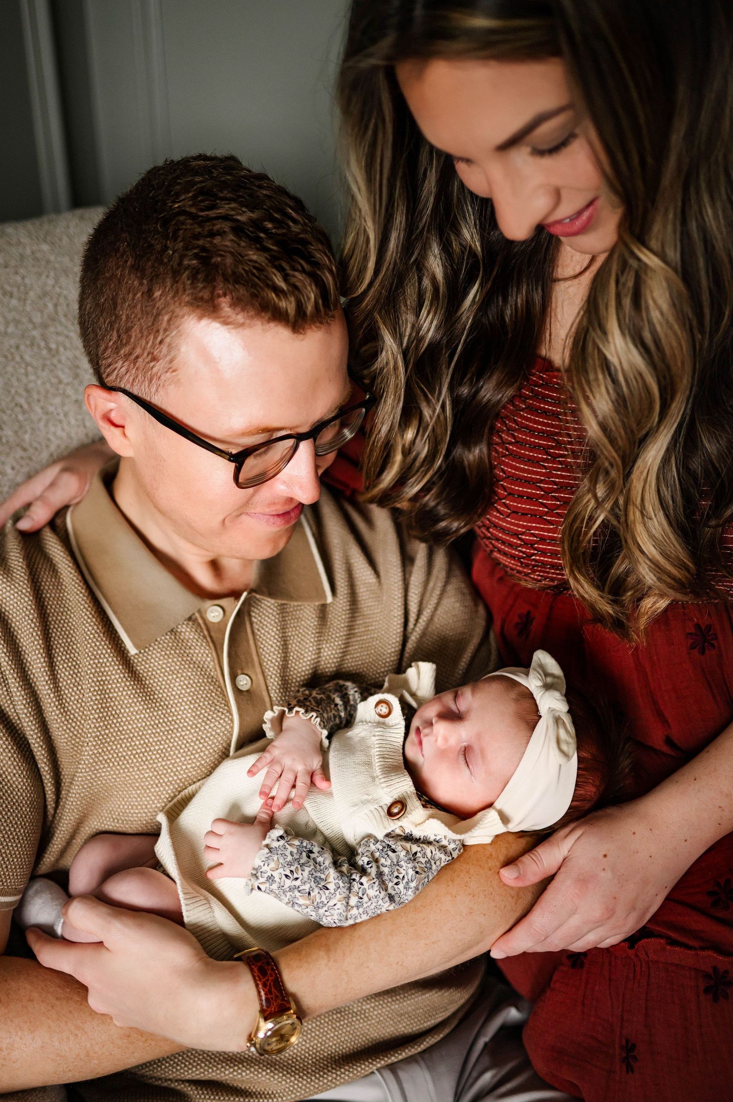 Young parents lovingly gaze at their sleeping newborn baby dressed in white in their home with durham nc newborn photographer
