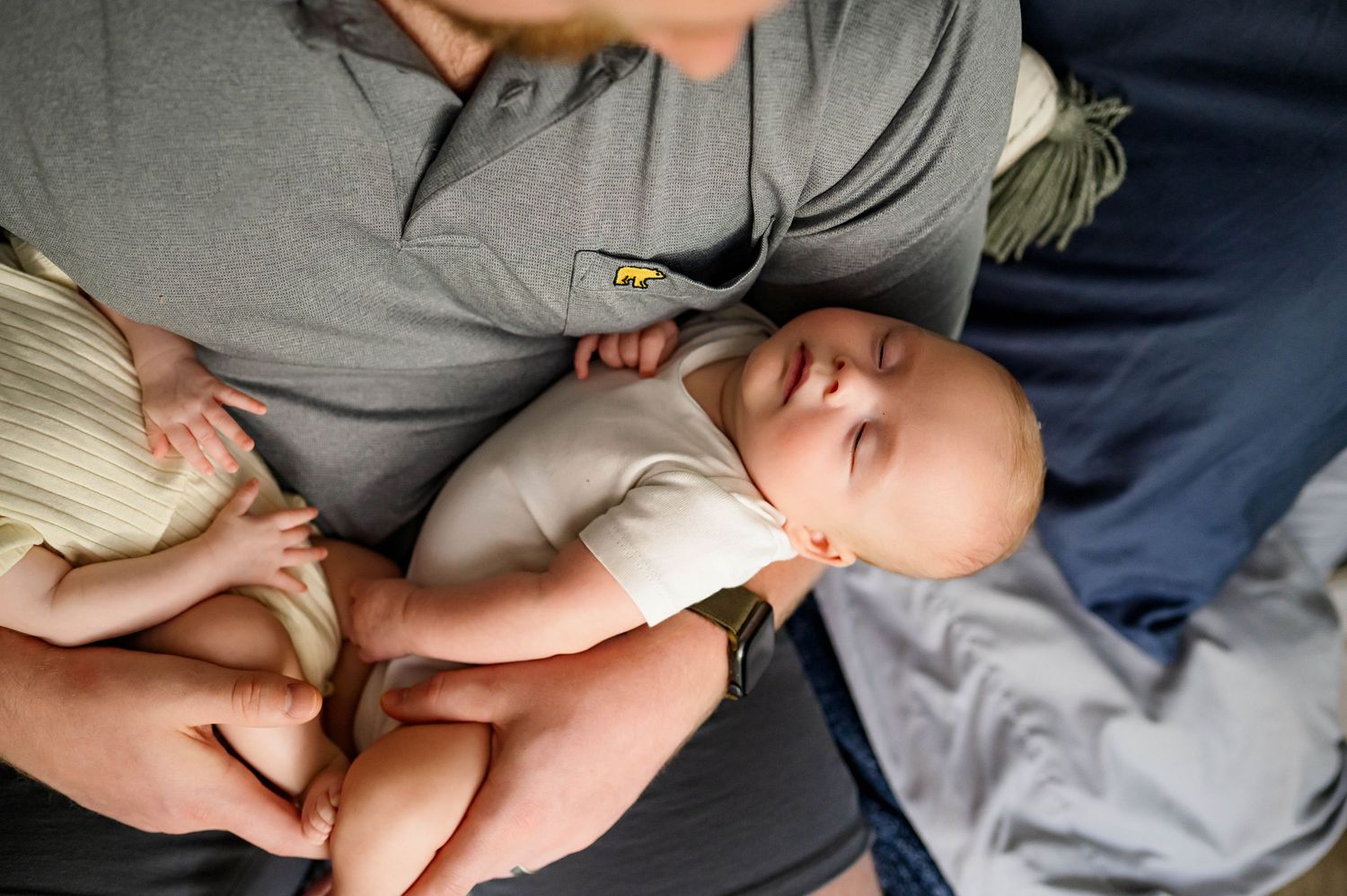 Baby sleeping peacefully on parent's lap in grey clothing while being gently cradled with wake forest newborn photographer