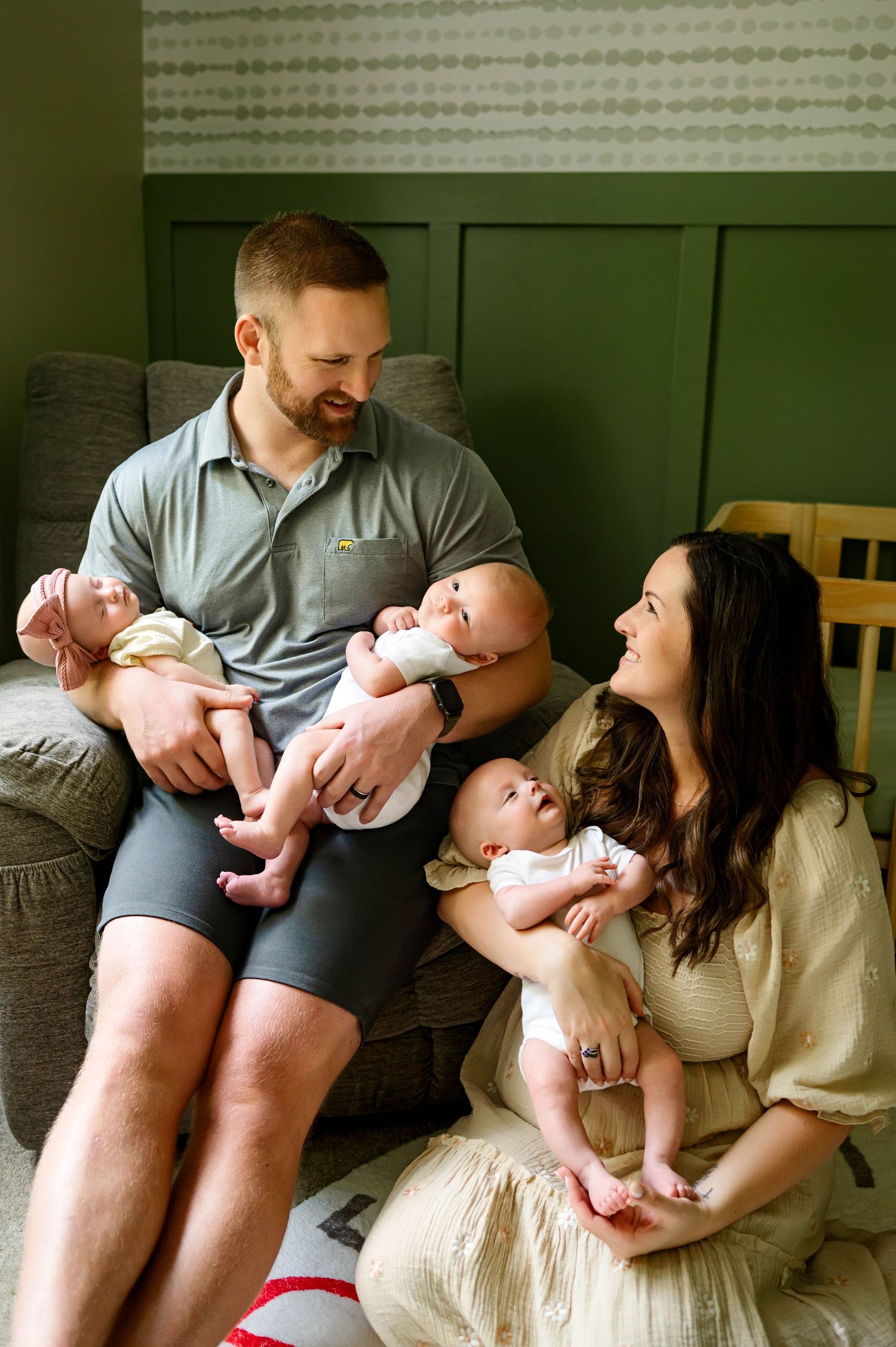 Parents smile at each other while holding their triplet newborns in their nursery with newborn photographer in raleigh
