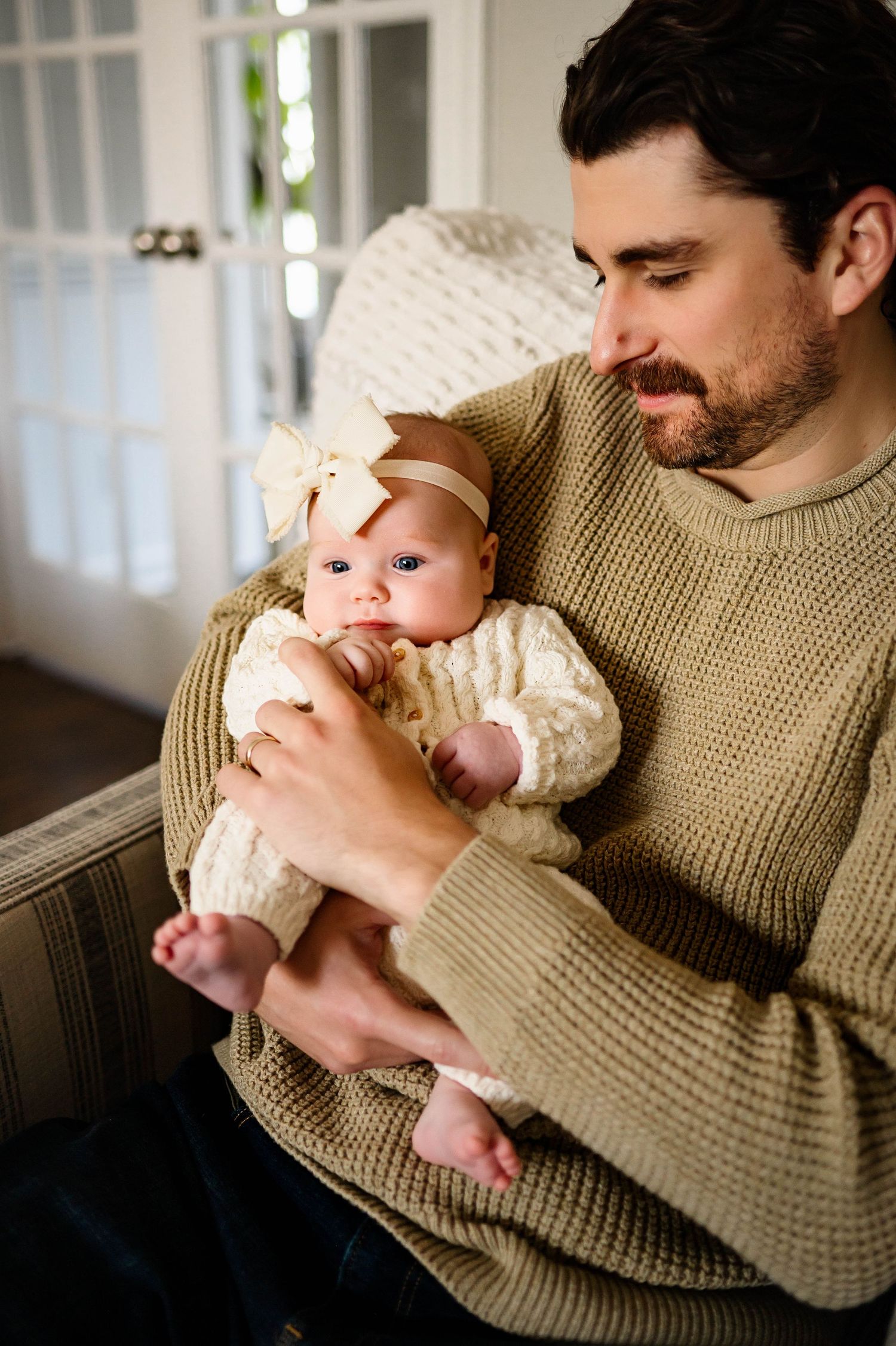 A tender moment captured as a father in a sweater cradles newborn daughter wearing a cream with best wake forest nc newborn photographer