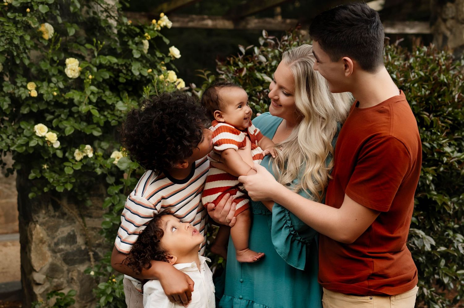 A loving family shares a tender moment together with newborn brother surrounded by roses with raleigh family photographer