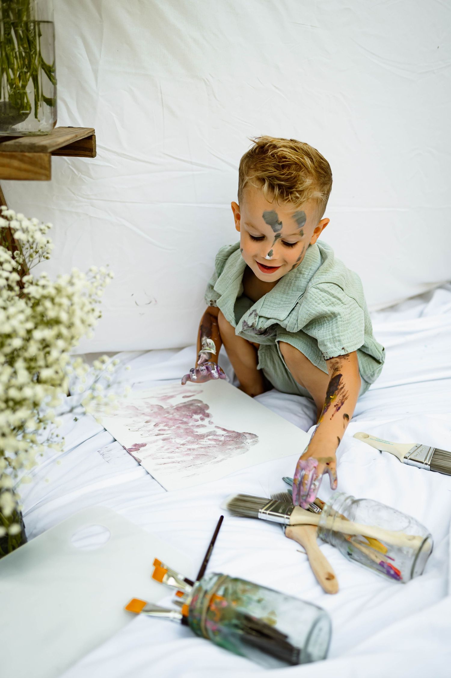 A paint-covered child in green clothing creates art with paintbrushes and art supplies with chapel hill family photographer