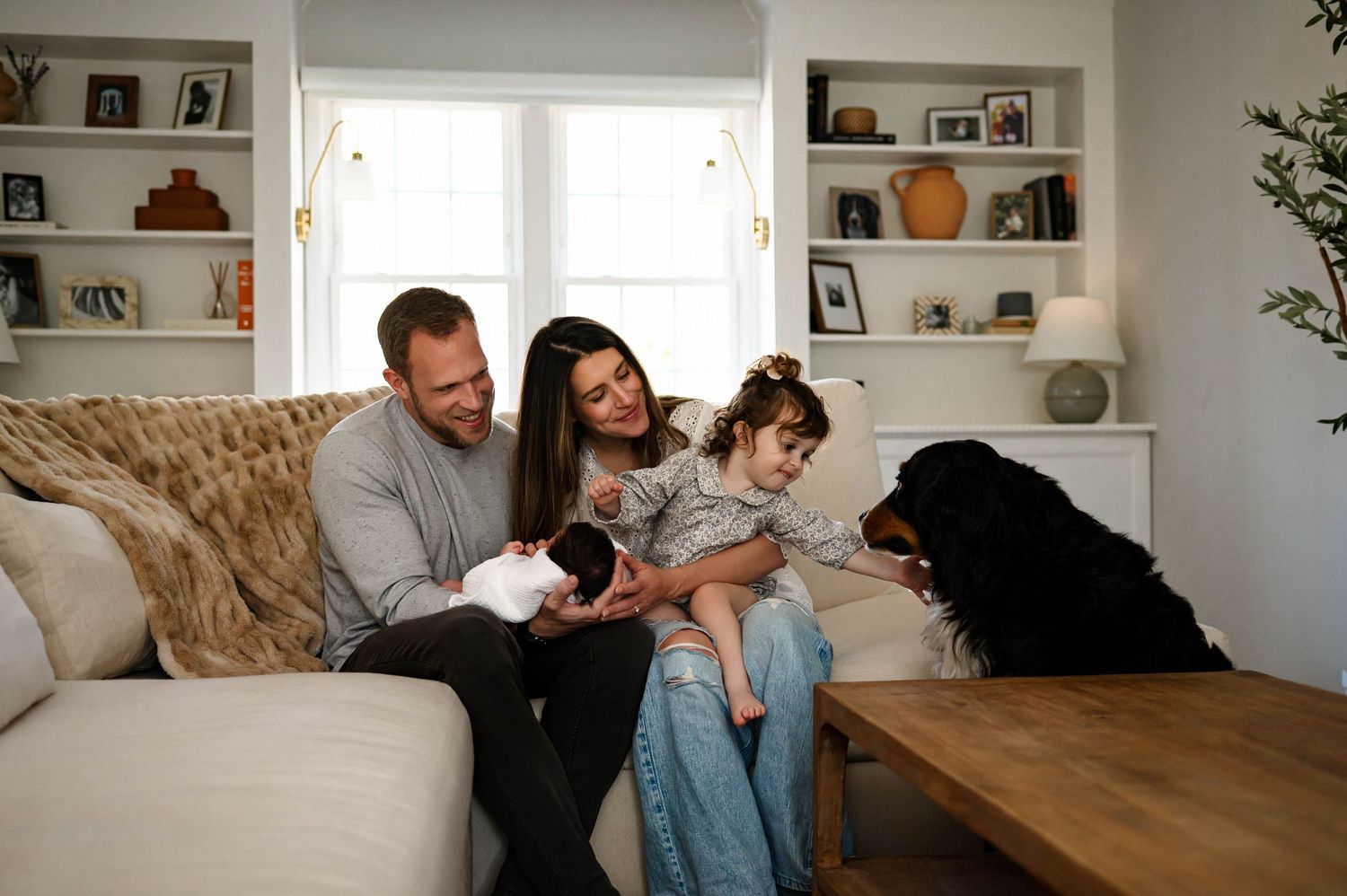 A family relaxes on a couch at home with their dog while surrounded by natural light with the best raleigh newborn photographer