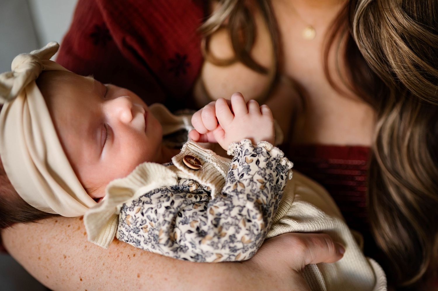 A sleeping baby wearing a flowered shirt rests peacefully in cradled arms while mother admires during newborn photography session raleigh