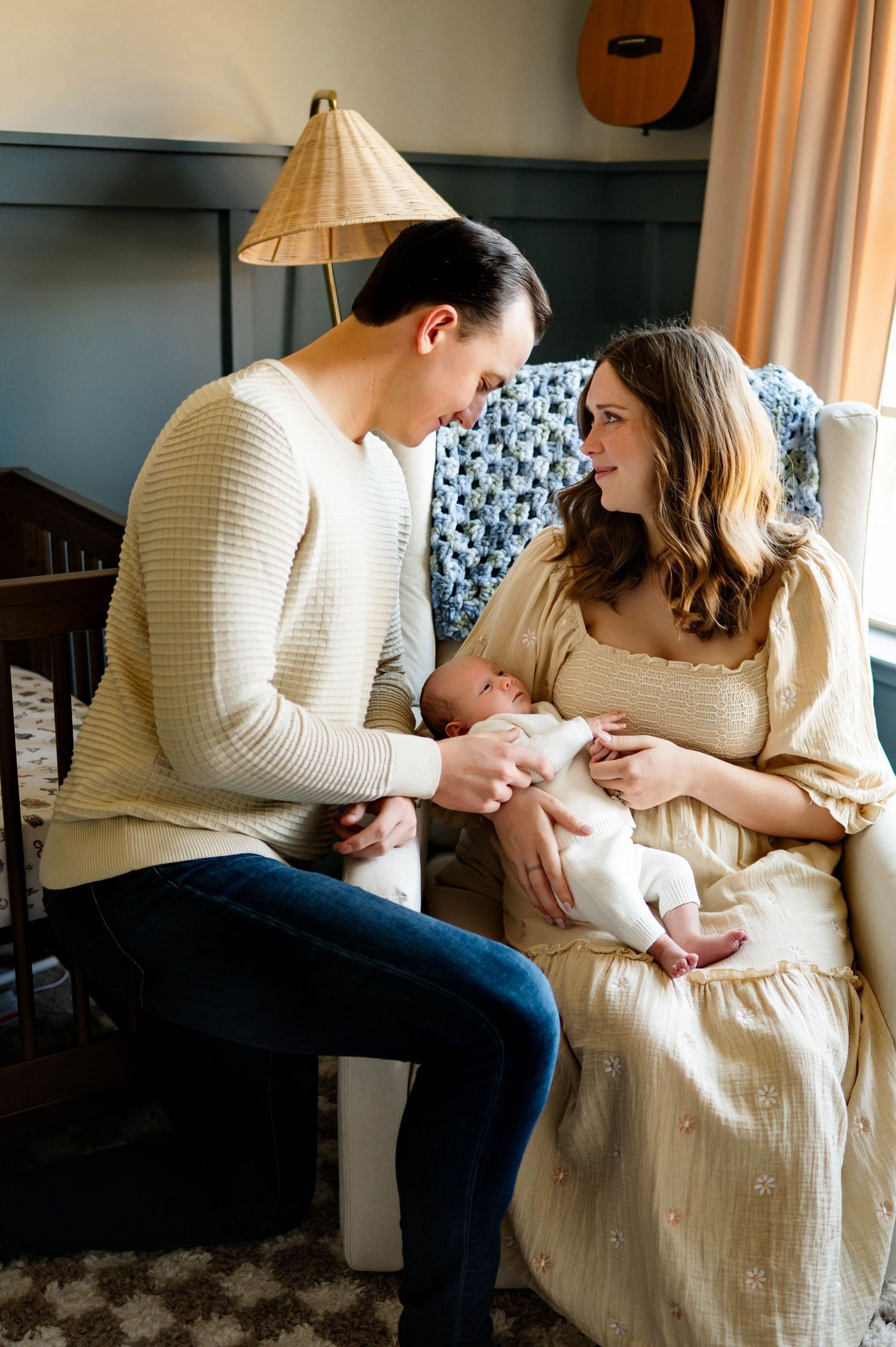 Couple in matching cream sweaters sitting together by a lamp while holding their newborn baby with the best newborn photographer raleigh