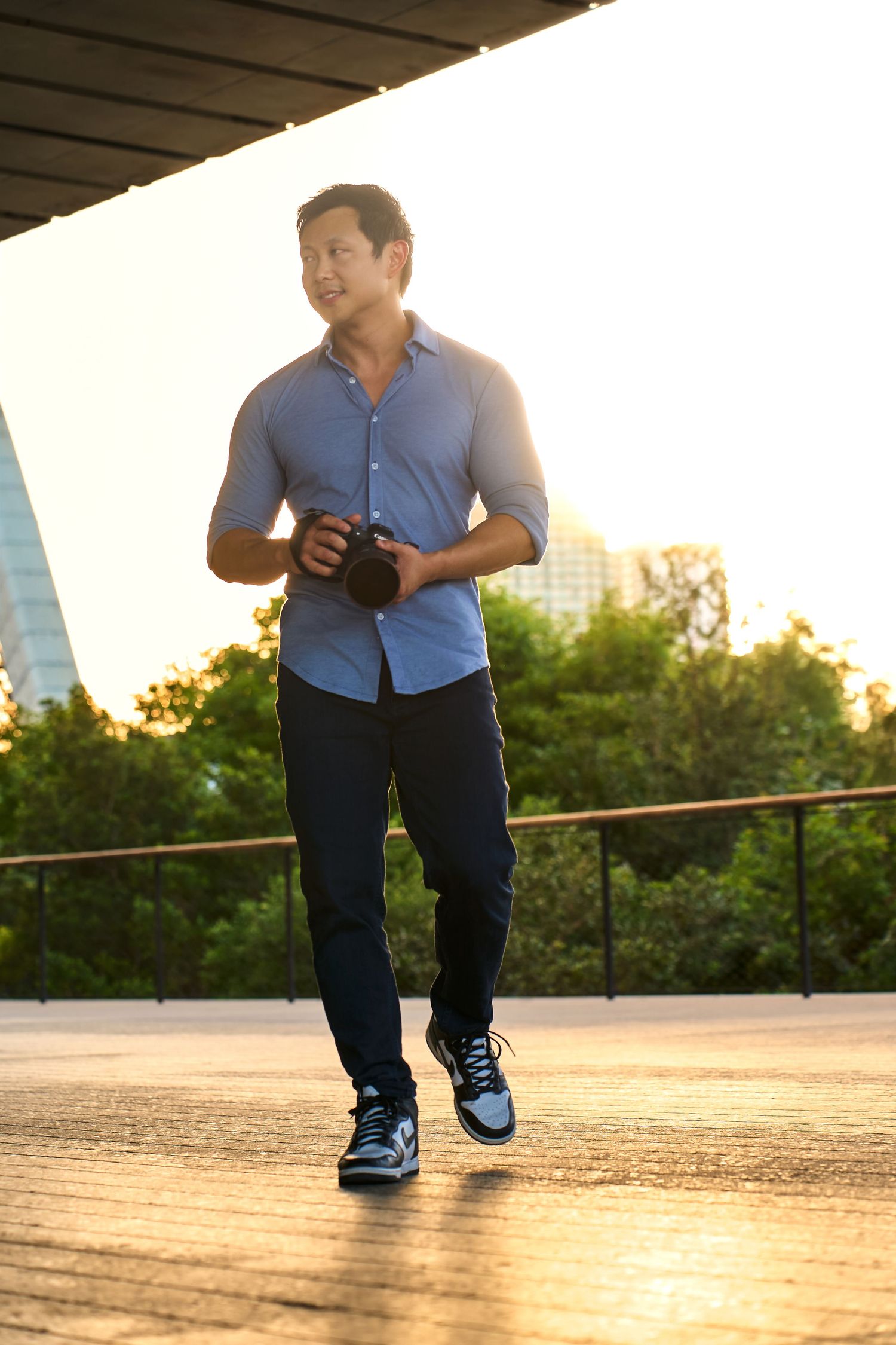 Chris Ha in blue shirt walking with camera during golden hour under urban overhang in Miami.