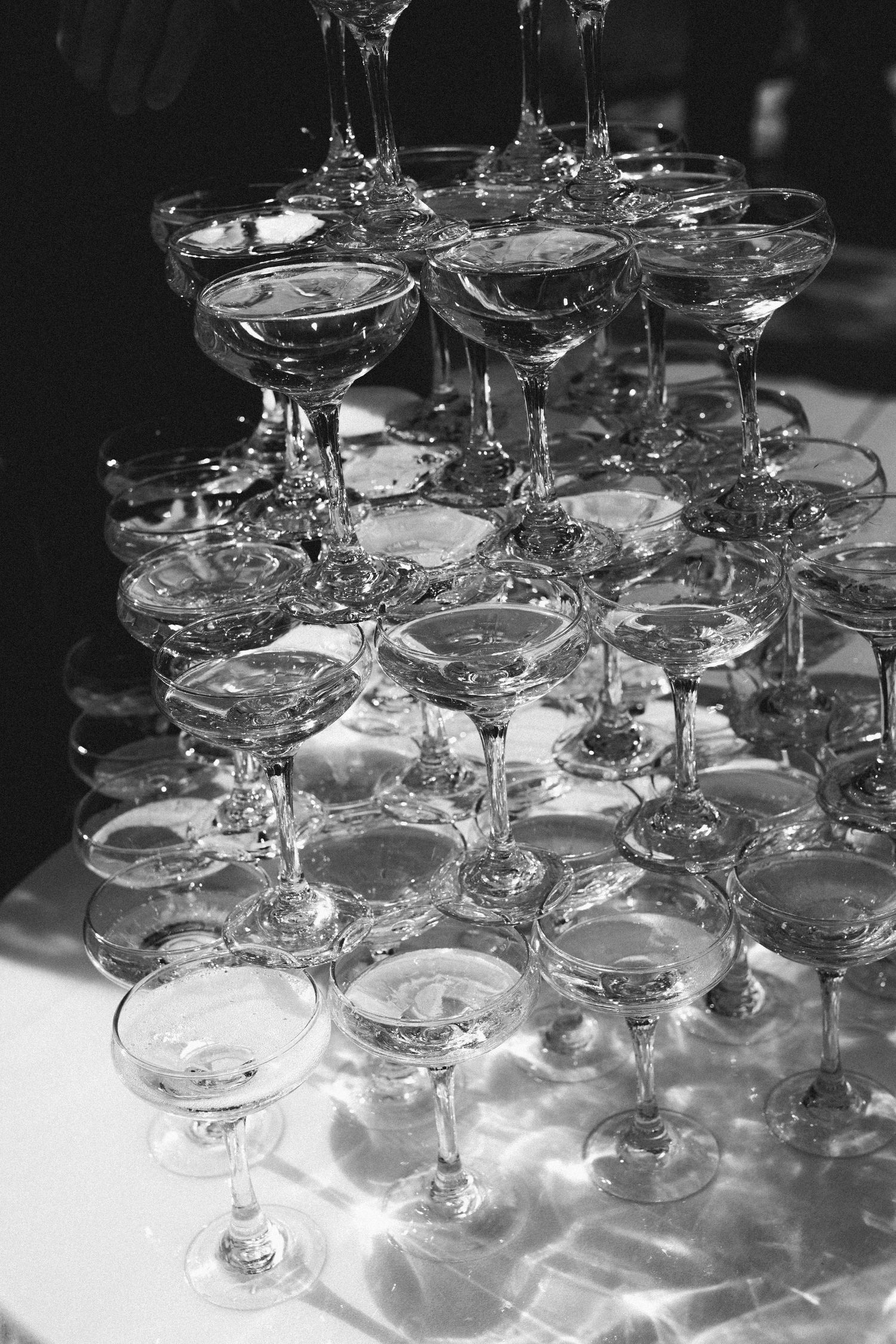 A black and white photograph of stacked champagne glasses arranged in a pyramid formation on a white tablecloth.