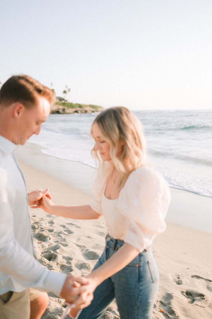 Joyful couple dancing and laughing together on sunny beach with waves in background.