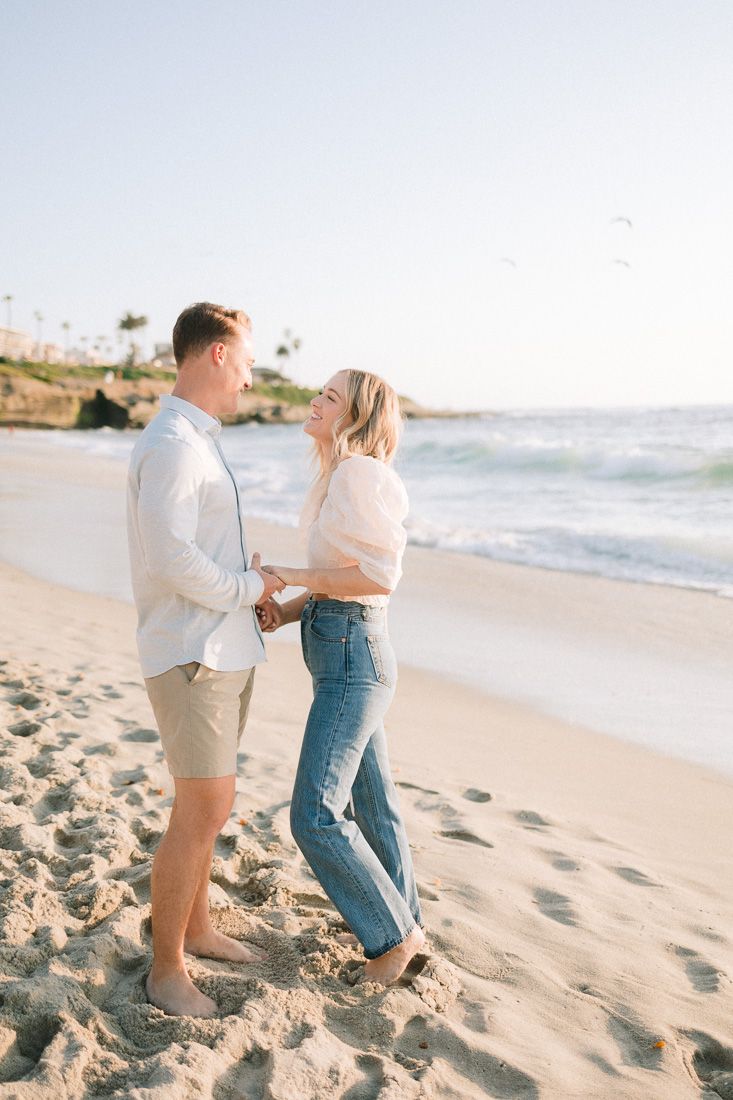 Tender moment between couple on sunny beach with coastal landscape in background.