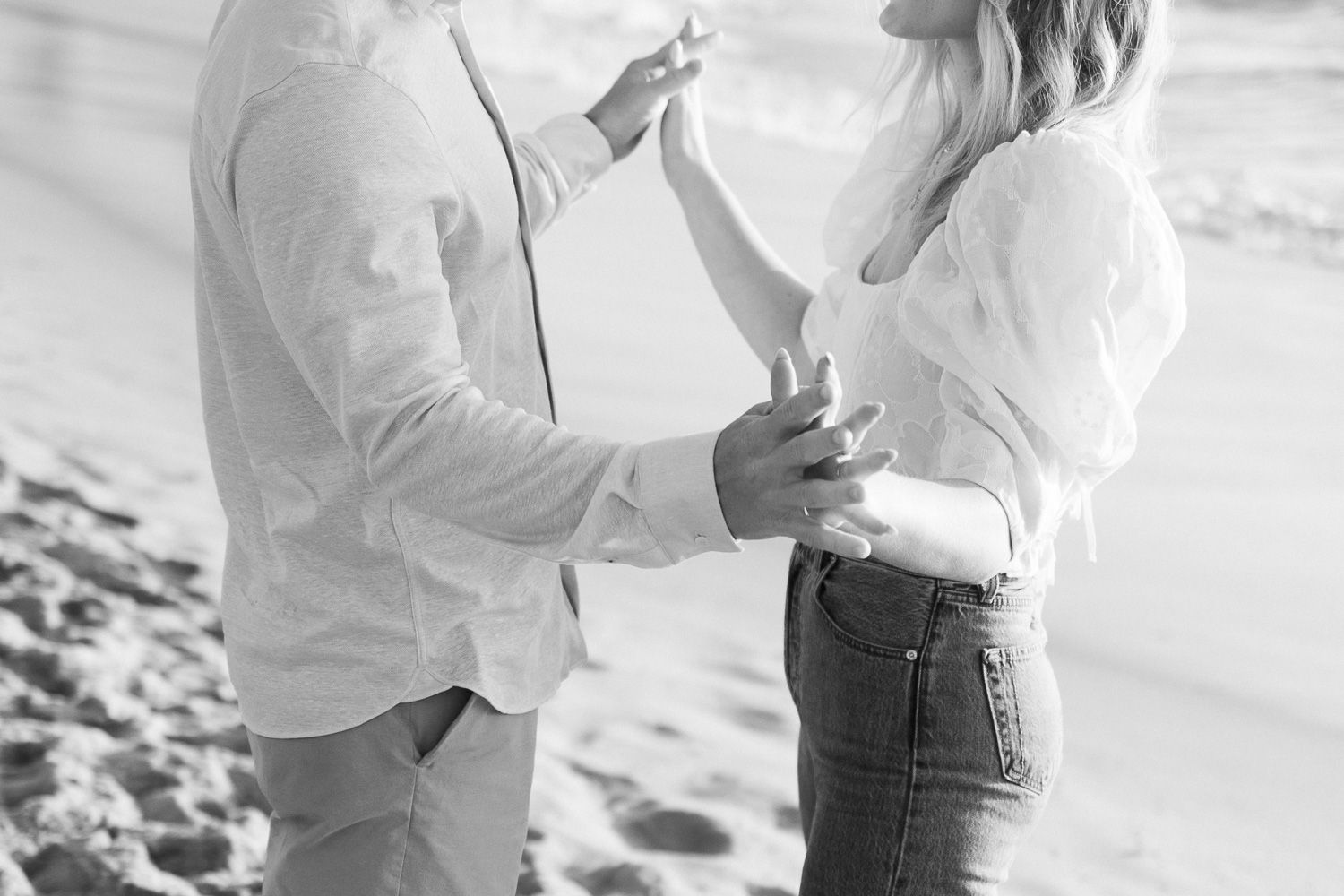 Black and white capture of intimate moment between couple on beach during sunset.