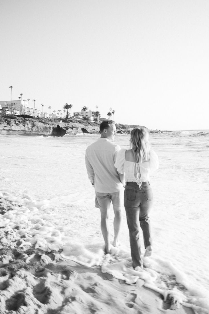 Black and white photo of couple enjoying a peaceful moment on beach with waves crashing nearby.