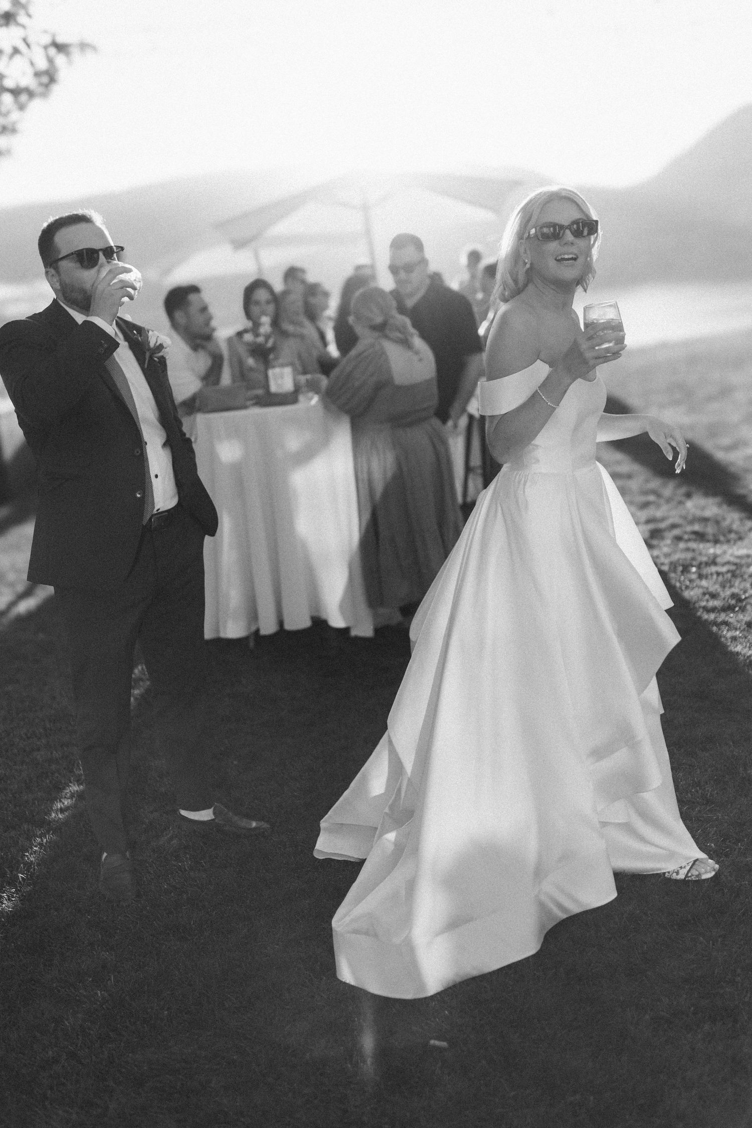 Black and white wedding photo of guests dancing and celebrating at an outdoor reception with mountains in background.