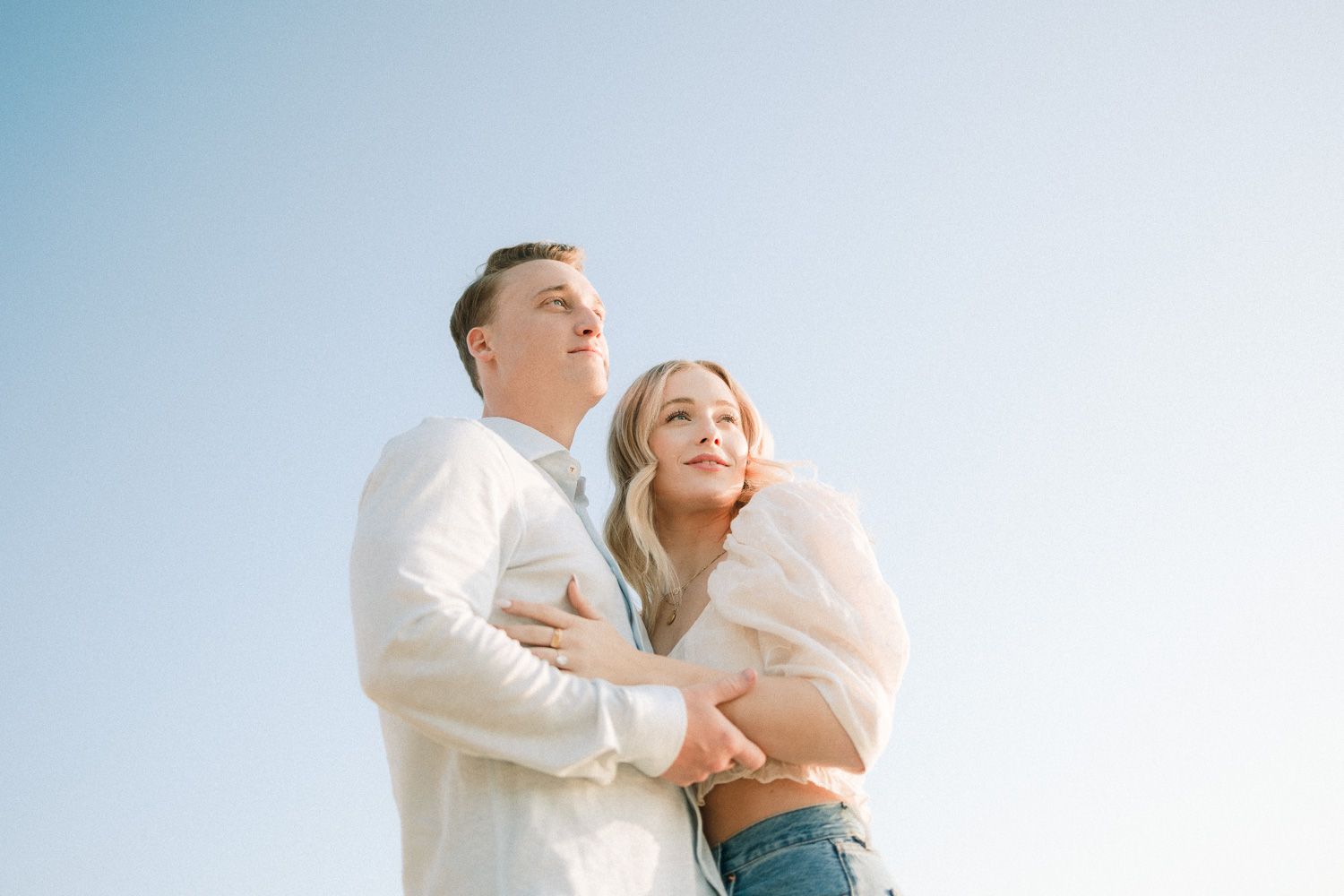 A couple embracing on the beach against a bright blue sky background.