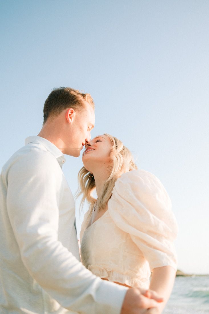 Intimate beachside moment with bright blue sky and ocean waves in background.