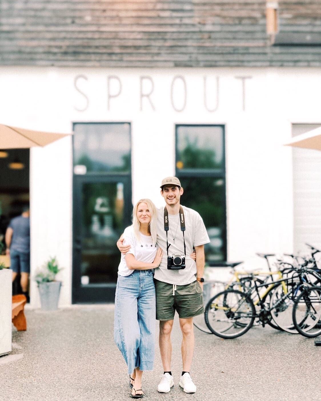 A couple stands outside Sprout cafe with bicycles parked nearby on a sunny day.