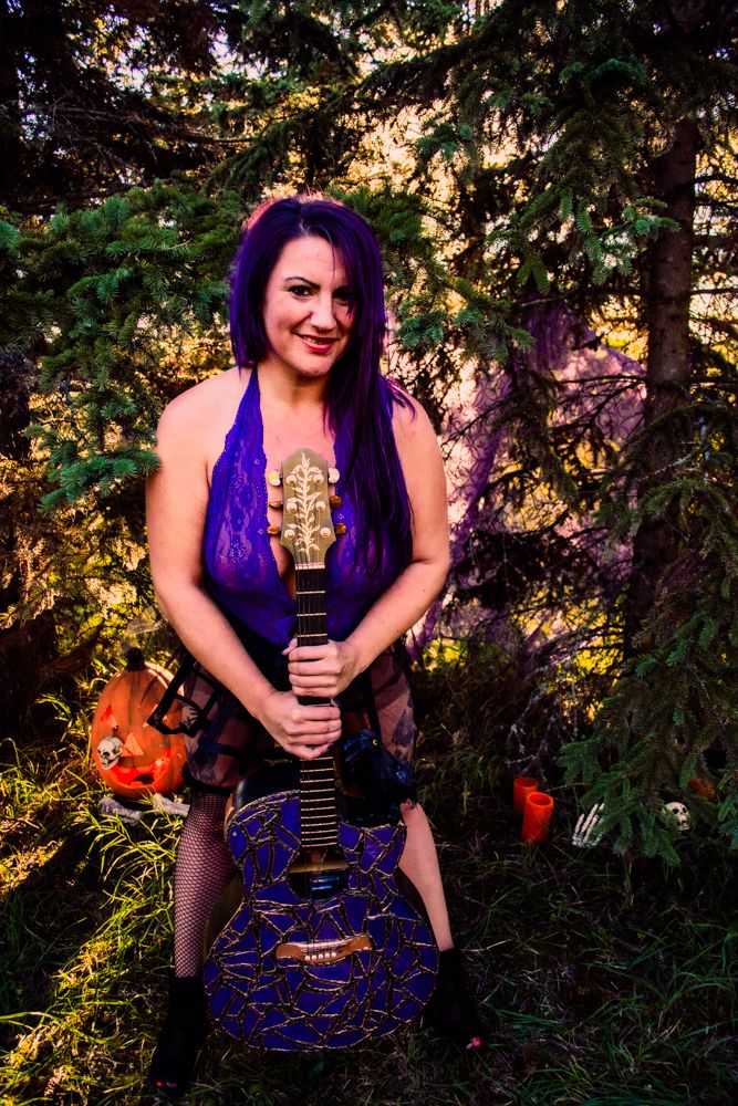 Purple decorated acoustic guitar in halloween themed outdoor photoshoot with autumn forest backdrop.