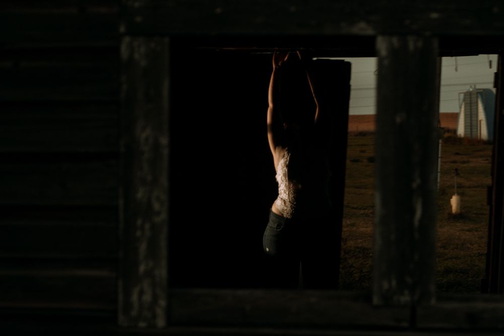 Silhouetted ballet dancer seen through dark window frame at dusk.