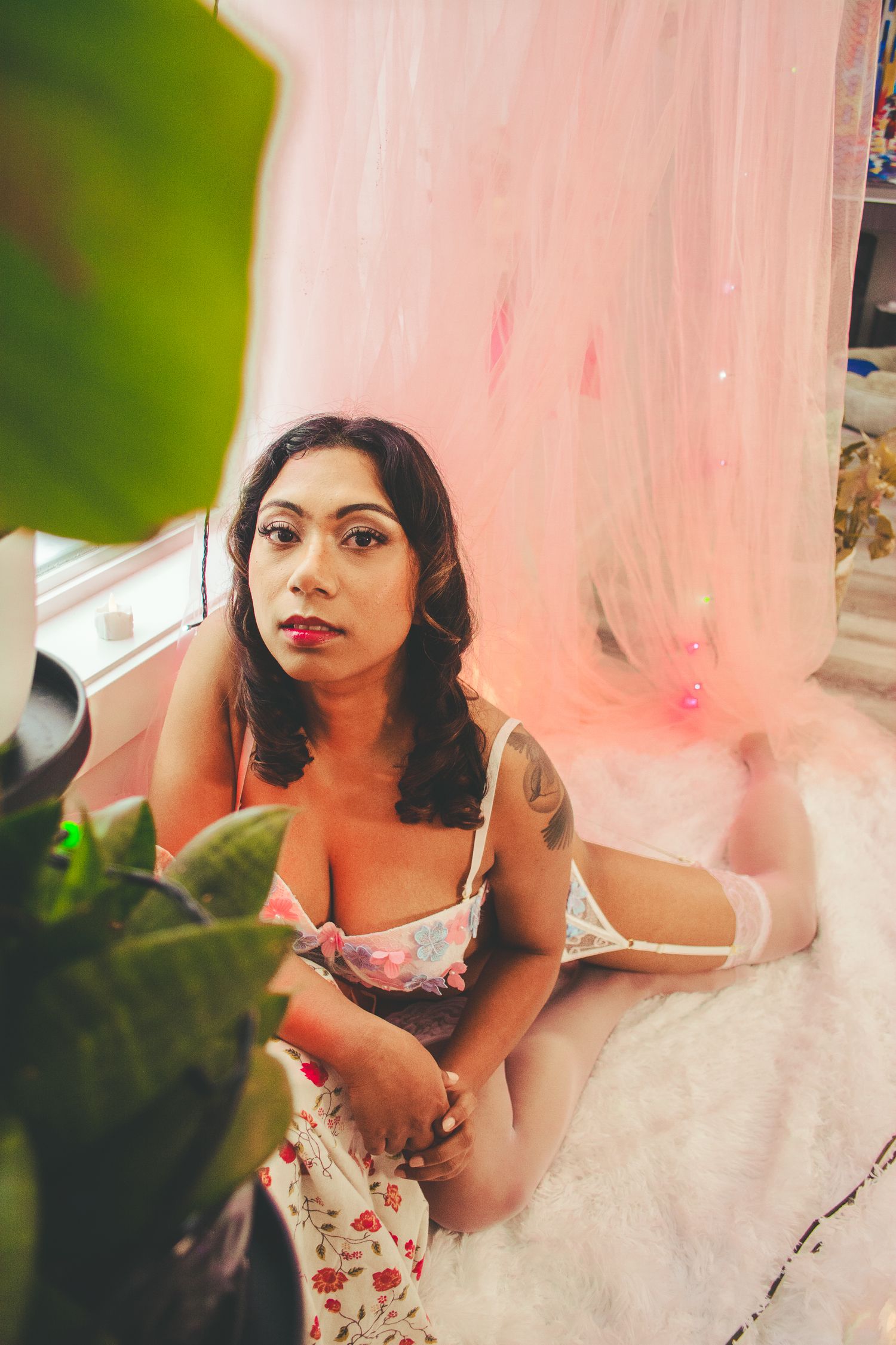 A boudoir photoshoot featuring soft pink tulle draping and indoor greenery.