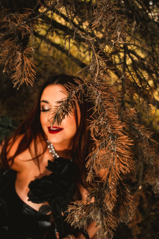 Artistic portrait through pine branches with golden sunset lighting.