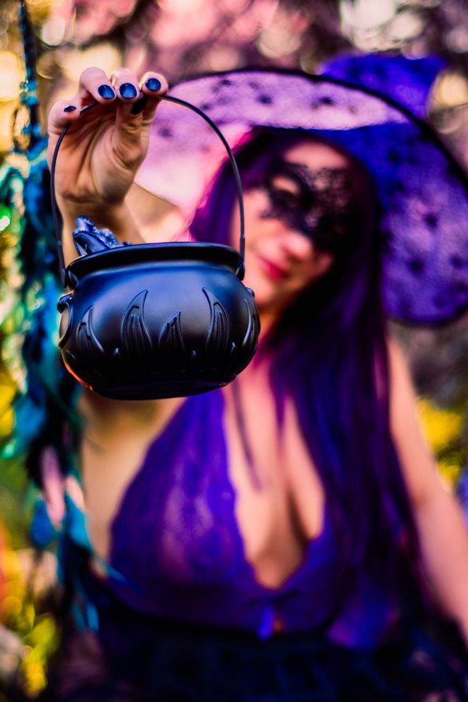 Black cauldron prop held against blurred purple and golden background in witch themed photoshoot.