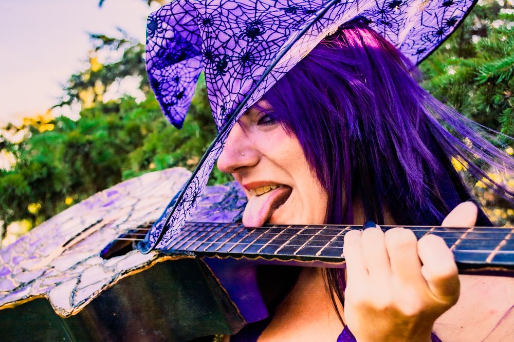 Close up of purple decorated acoustic guitar with spiderweb pattern witch hat in outdoor setting.