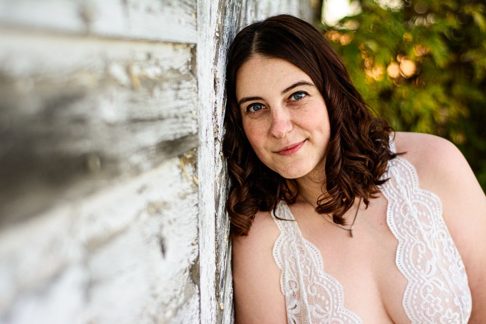 Portrait in white lace leaning against rustic white wall with natural lighting.