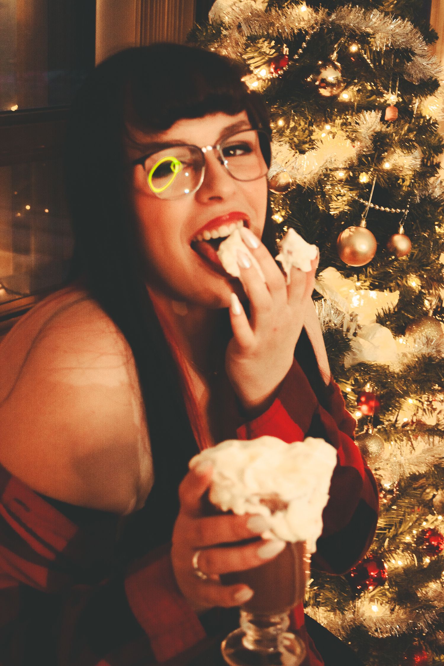 Person enjoying a holiday beverage in front of a decorated Christmas tree with warm lighting.