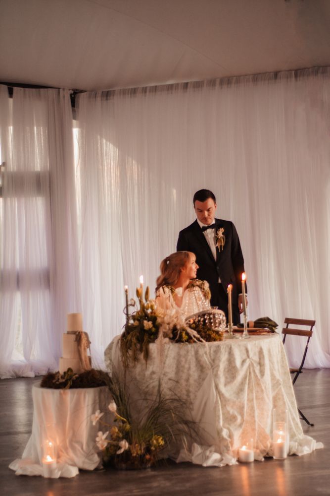 Elegant sweetheart table setting with white linens and candlelight at indoor wedding reception.