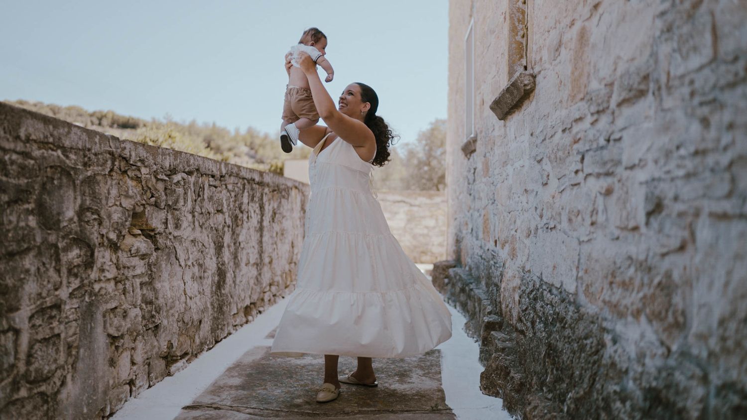 A tender wedding moment captured between two people on a stone walkway with sunlit ancient walls surrounding them.