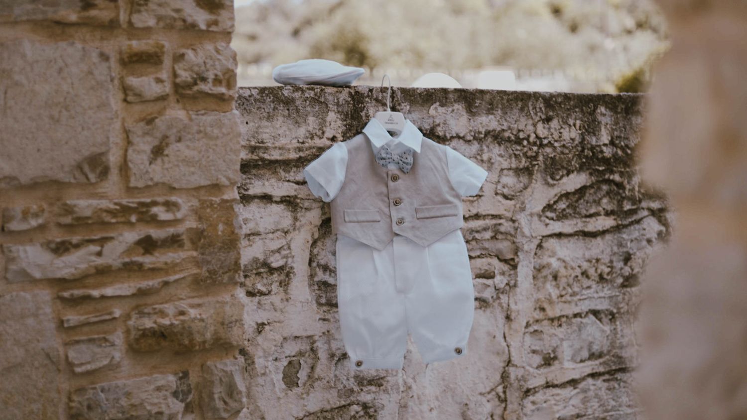 White lace wedding dress hanging on a rustic stone wall in soft natural lighting.