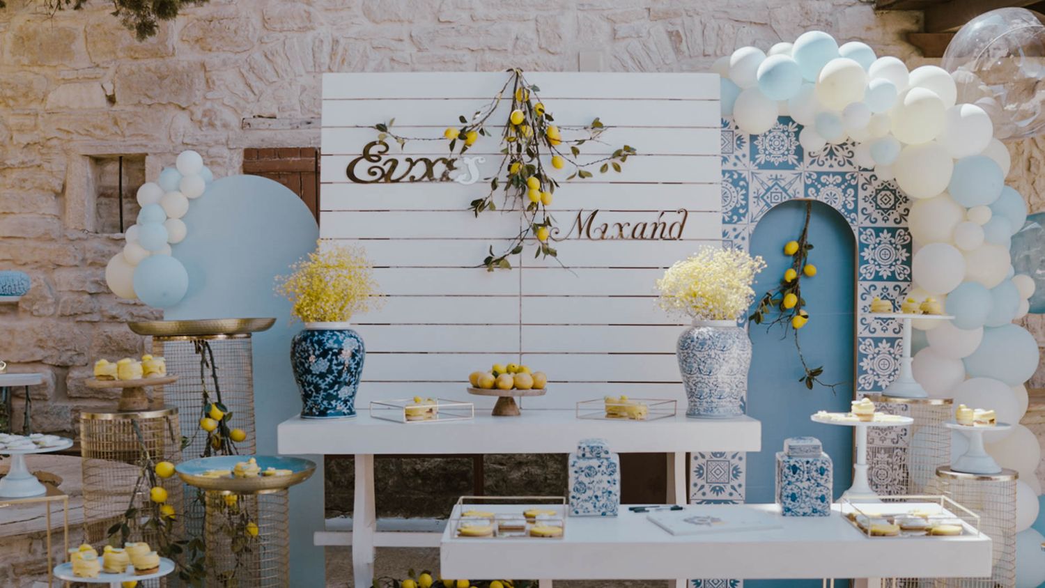 Elegant wedding backdrop with blue and white balloon arch, rustic stone wall, and floral decorations.