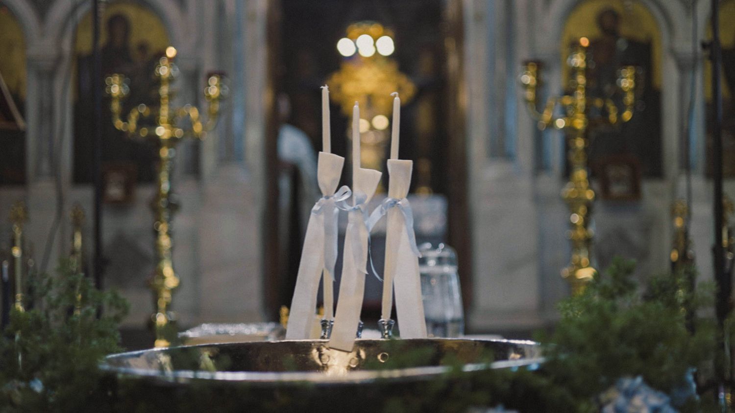 White candles burn in an ornate church interior with golden chandeliers and decorative architecture.