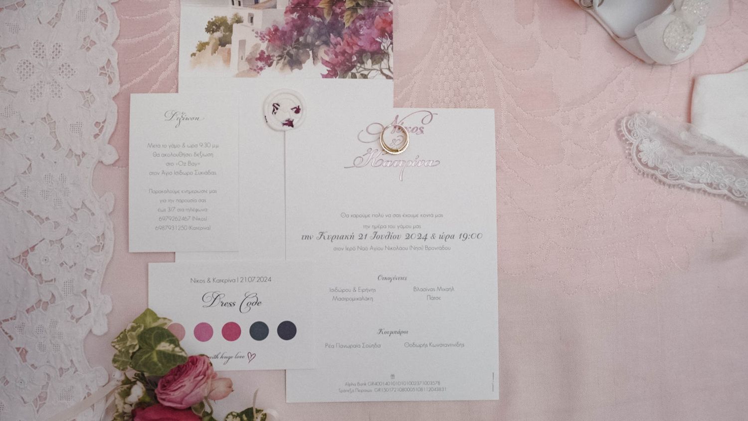A wedding invitation with color palette swatches lies on a pink surface with floral decorations and ring details.