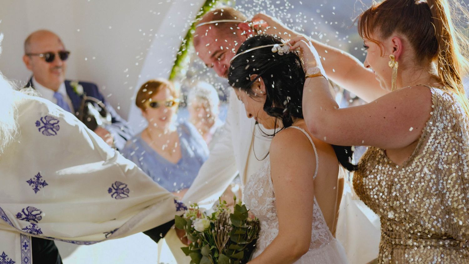 Wedding party members pour champagne over a joyful guest during a celebratory moment at an outdoor reception.