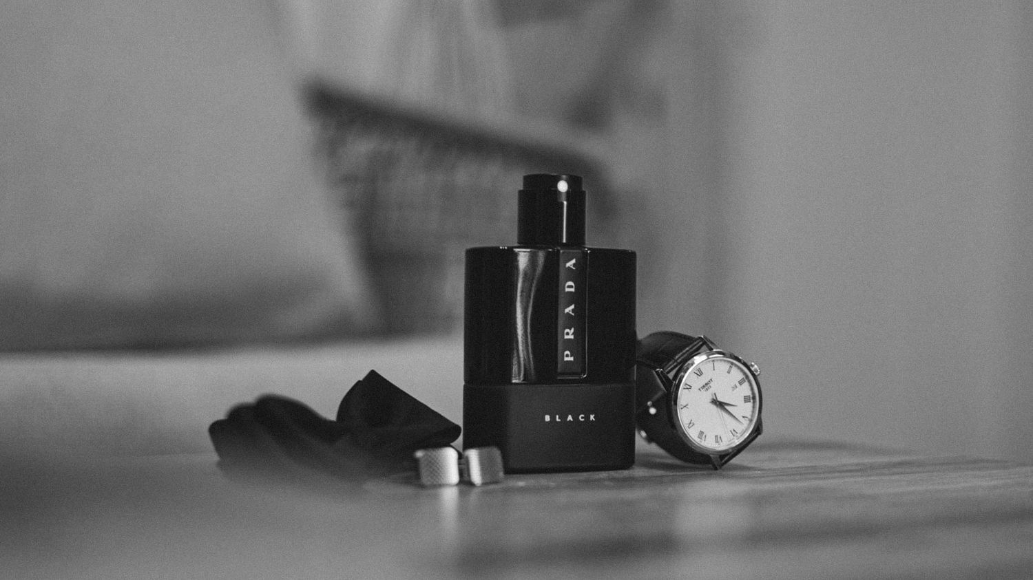 A black perfume bottle sits elegantly next to a classic analog watch on a reflective surface.