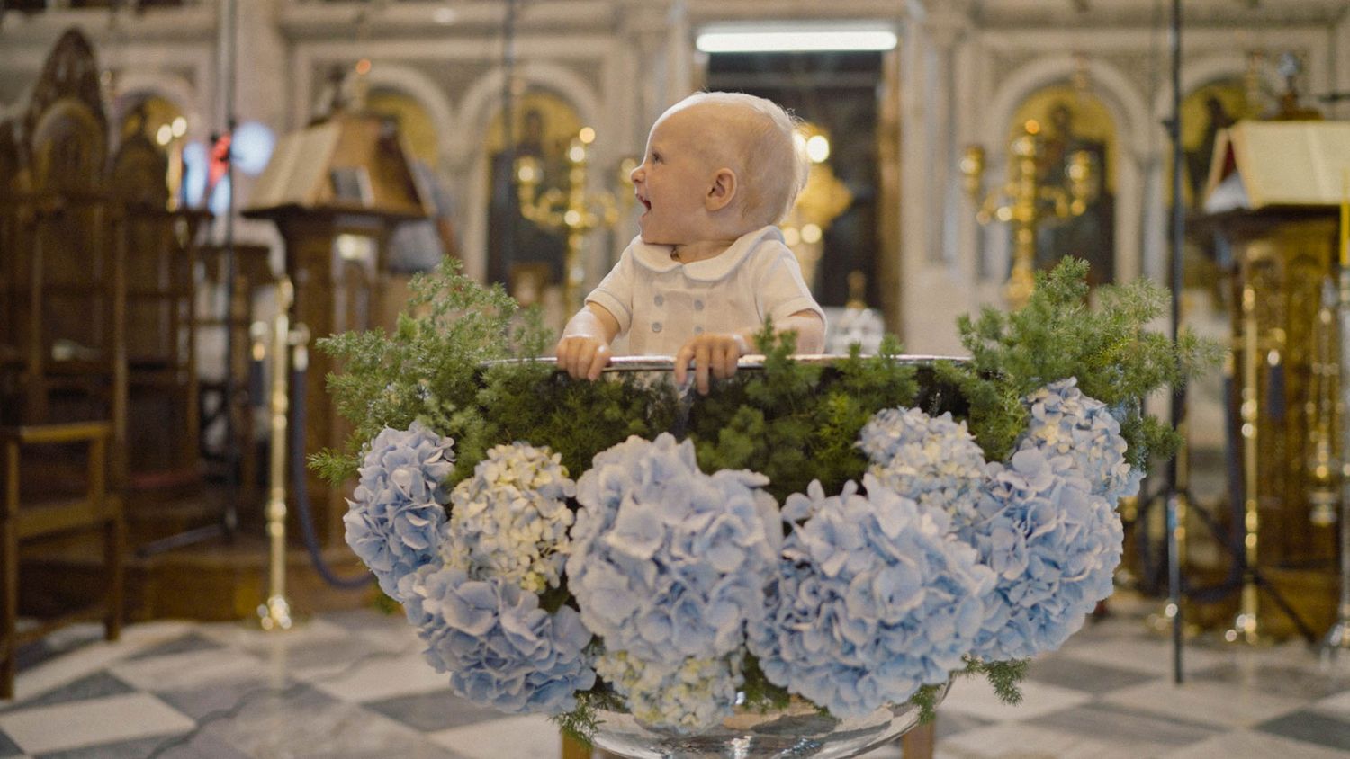 A cherub bust surrounded by blue hydrangeas in an ornate church setting with golden decorative elements in the background.