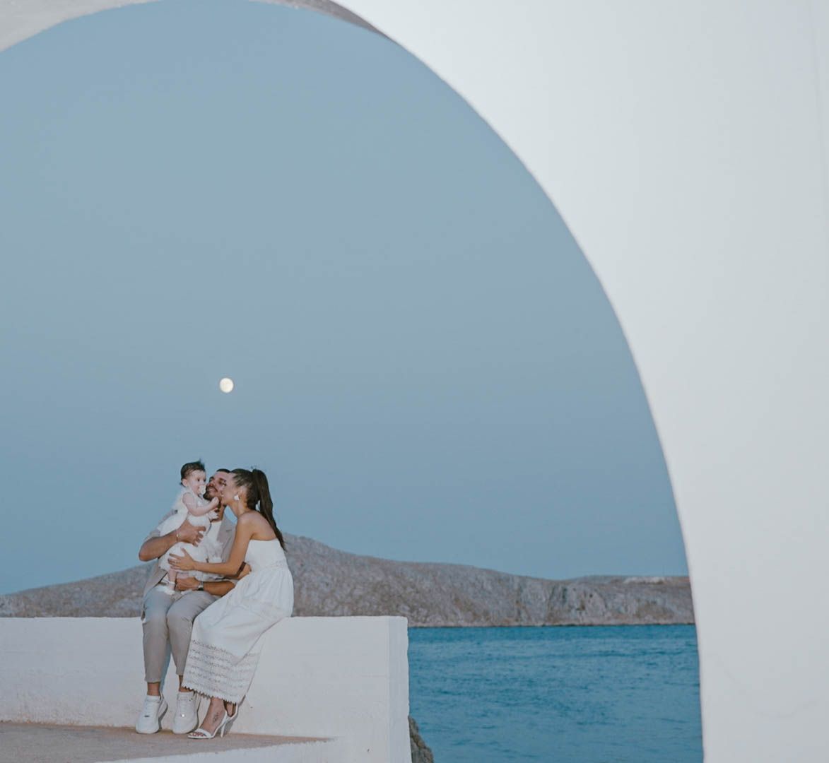 A couple shares a romantic moment in a white archway overlooking the Mediterranean Sea in Santorini, Greece.