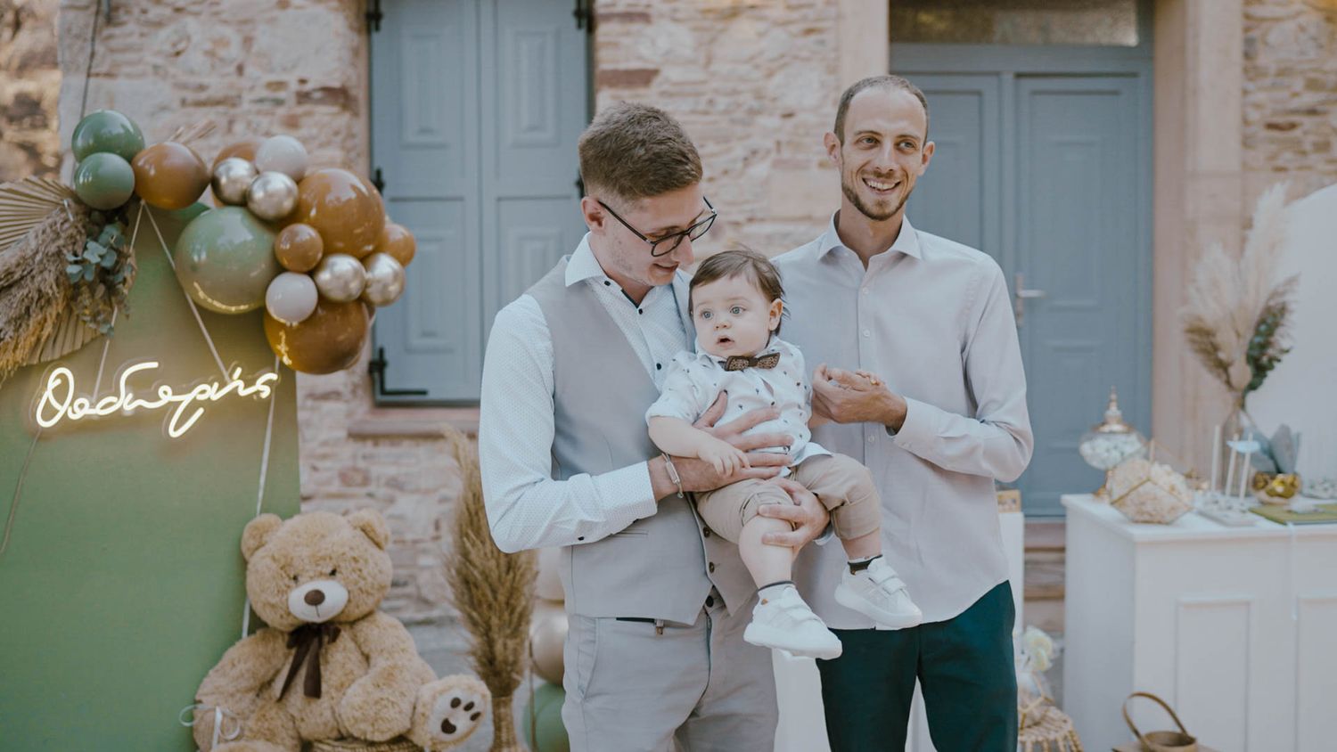 A stylish family gathering at a baby shower celebration with balloon decor and a teddy bear against blue doors.