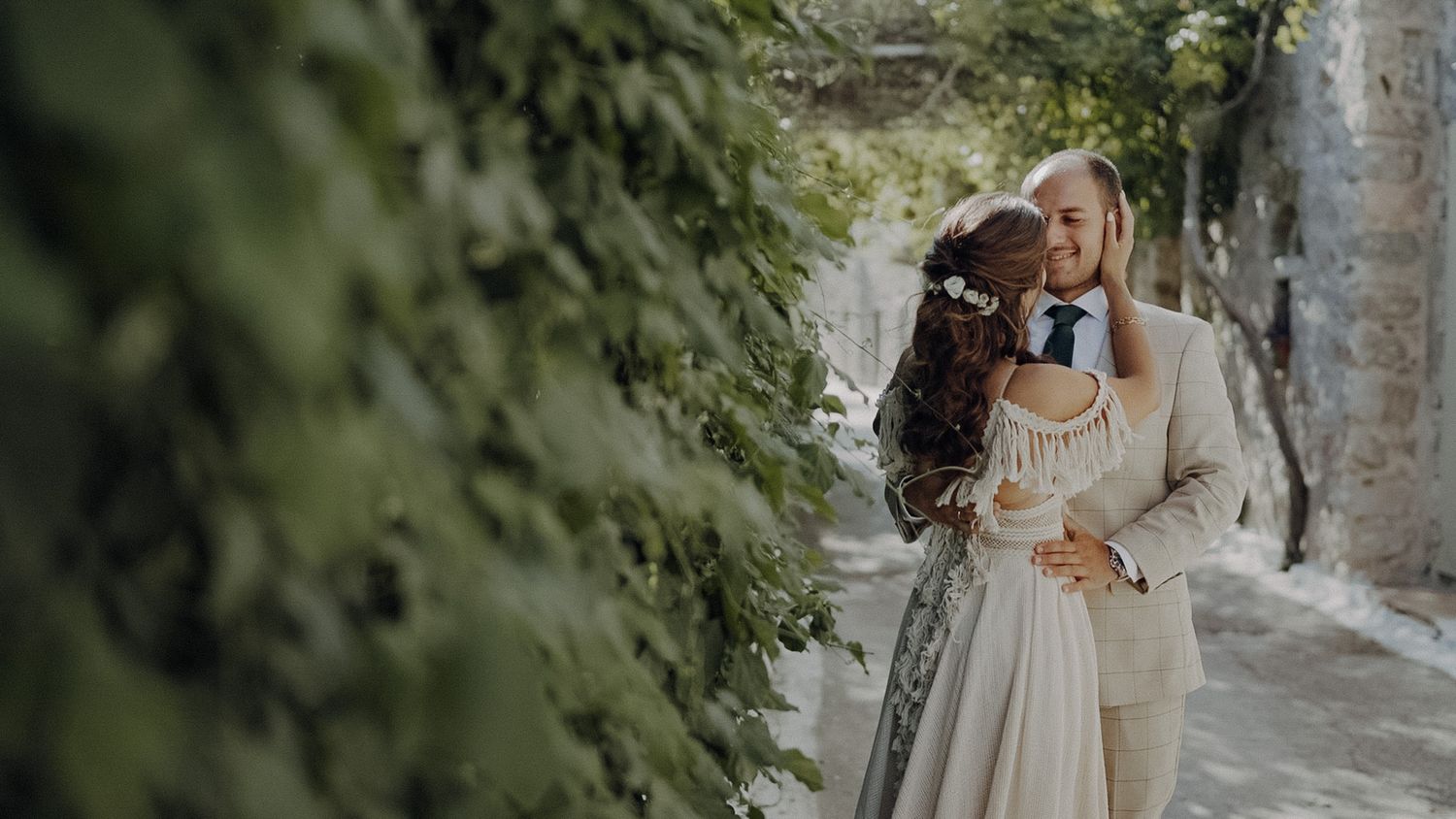A romantic moment captured in a stone alley with ivy-covered walls and natural lighting.