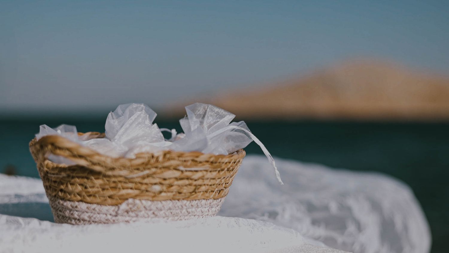 Small woven basket filled with white tulle fabric resting on a textured surface with blurred mountains in background.
