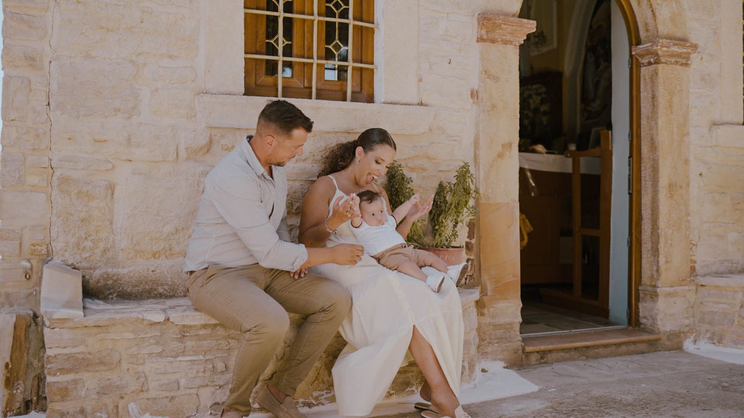 A couple sits on stone steps in warm sunlight outside a rustic building entrance.