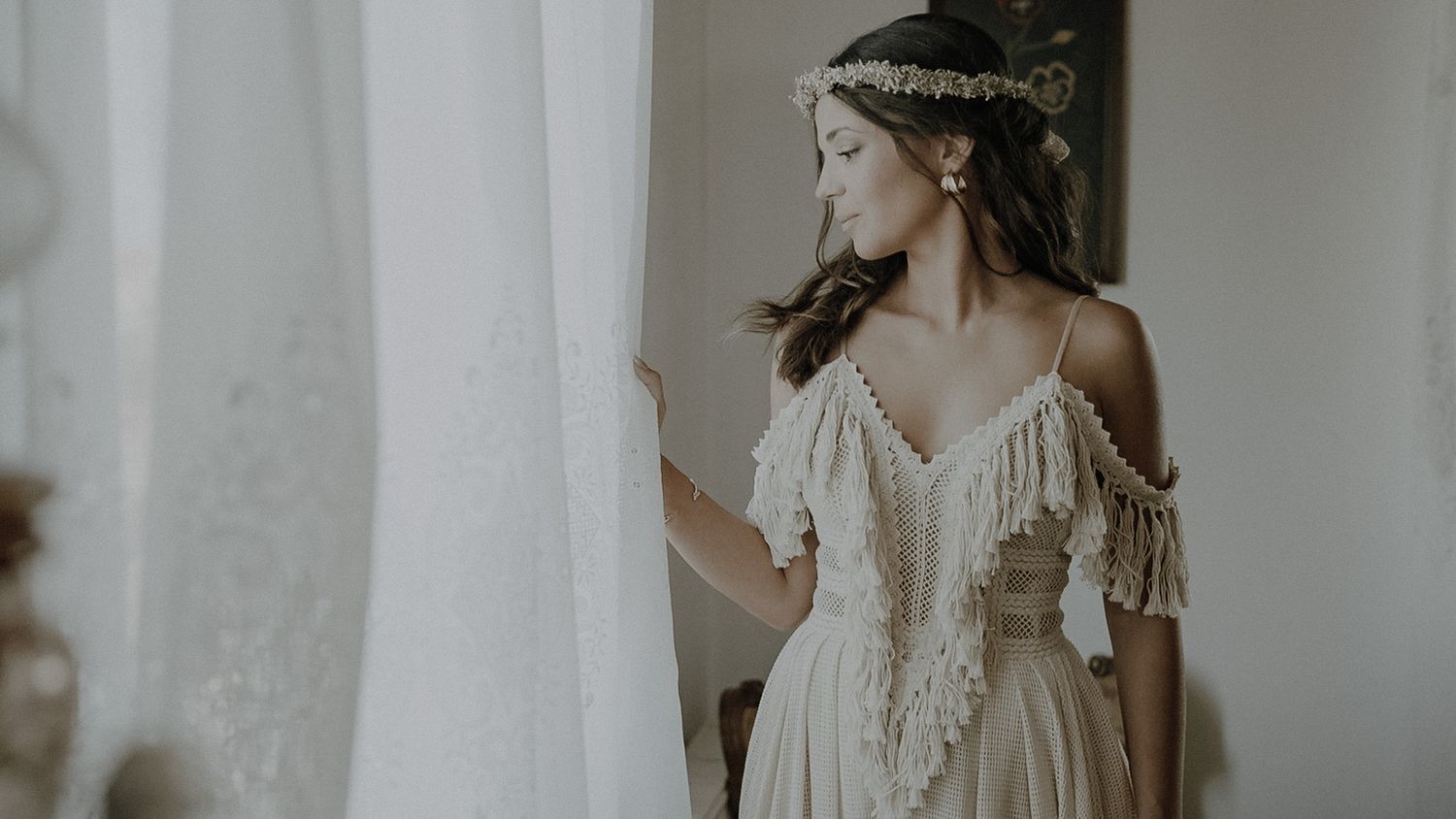 Ethereal bridal portrait with flowing dress and delicate headpiece against white curtains.