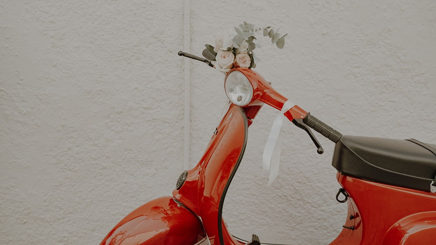 Vintage red Vespa scooter decorated with wedding flowers against white wall.