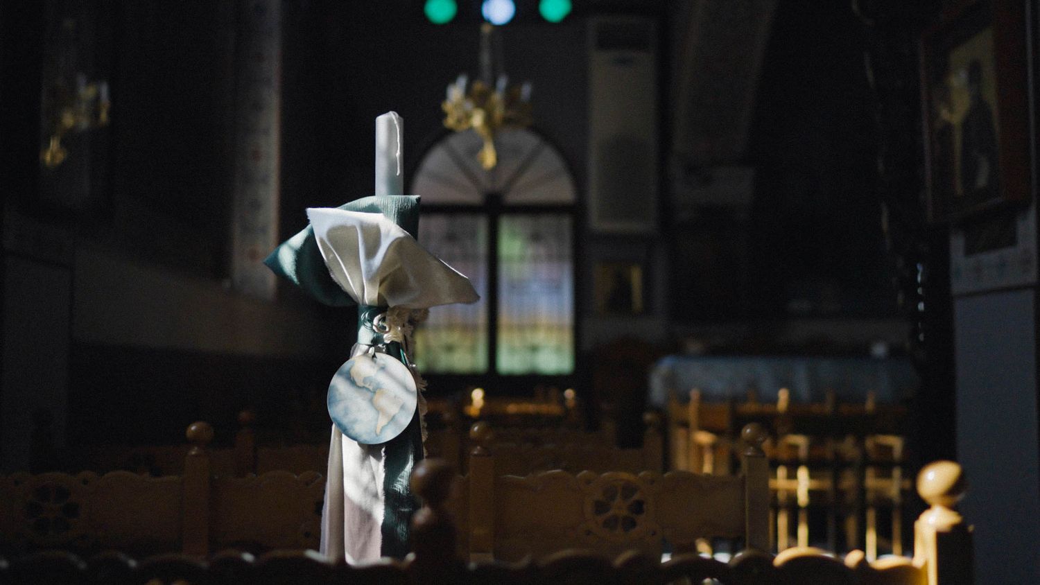 Small decorative canister on a wooden pole inside a dark church or cathedral with stained glass windows in background.