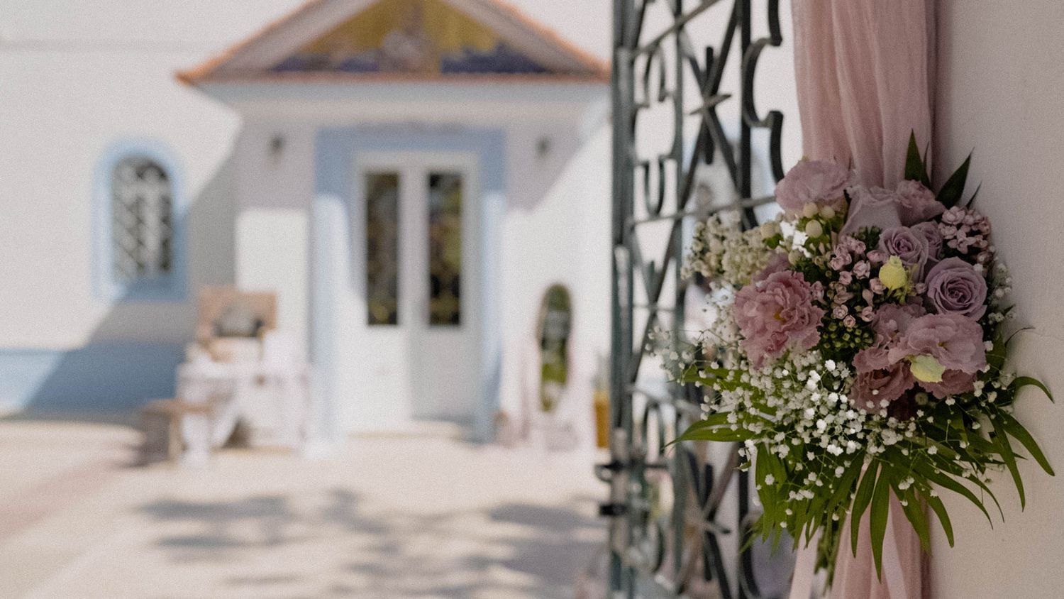 Beautiful floral arrangement with pink and purple blooms adorns a wrought iron gate entrance to a white Mediterranean villa.